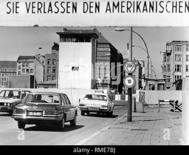 Auto Verkehr am Grenzübergang für Ausländer am Checkpoint Charlie in der Friedrichstraße in Berlin. Über dem Schild "Sie verlassen den amerikanischen Sektor". In der Mitte ist ein Wachturm der DDR-Grenzanlagen. Undatiertes Foto, vermutlich aus den 70er Jahren. Stockfoto