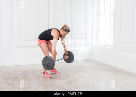 Seitenansicht Porträt der jungen athletischen schönen Bodybuilder Frau in rosa Shorts und schwarzen Top falsch hockt und Training im Fitnessraum mit der Ba Stockfoto