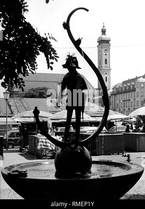 Die karl-valentin-Brunnen auf dem Viktualienmarkt in München. Im Hintergrund die Heilig-Geist-Kirche (Undatiertes Foto). Stockfoto