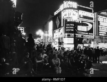 Piccadilly Circus in London: Bilder zeigt, beleuchtete Werbung (Wrikley's Kaugummi, personna) und Jugendliche sitzen auf der Straße (Undatiertes Foto). Stockfoto