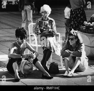 Zwei Mädchen (links Cecilia Blanco D. und rechten Alejandra Blanco M. aus Mexiko) mit Sonnenbrille auf dem Boden und ein älterer (Olivia Blanco) mit einer Broschüre, die auf dem Marienplatz in München, Juni 1986. Stockfoto