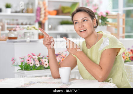 Porträt der schönen jungen Frau zeigt nach links, während sie Tee trinken. Stockfoto