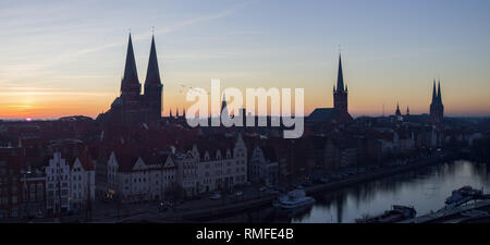 15. Februar 2019, Schleswig-Holstein, Lübeck: Die Sonne über der Hansestadt, die Stadt der sieben Türme. Von links die Marienkirche, drei Punkte auf das Rathaus, die St.-Aegidien-Kirche, der Petrikirche und dem Dom zu Lübeck. Die Trave fließt in den Vordergrund. Foto: Rainer Jensen/dpa Stockfoto