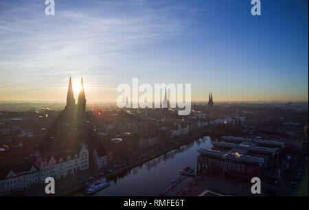 15. Februar 2019, Schleswig-Holstein, Lübeck: Die Sonne über der Hansestadt, die Stadt der sieben Türme. Von links die Marienkirche mit ihren Schatten, drei Punkte auf das Rathaus, die St.-Aegidien-Kirche, der Petrikirche und dem Dom zu Lübeck. Die Trave fließt in den Vordergrund. Foto: Rainer Jensen/dpa Stockfoto