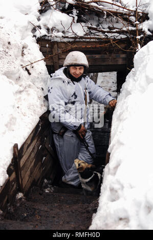 Januar 1, 2006 - Donezk Donezk Volksrepublik (DPR) D, Ukraine - EIN DPR Soldat gesehen warten in einem Schützengraben an der Front mit einem der Bereiche 'Angenommen' Hunde, sein Lächeln die guten Geister diese Männer haben zeigt. Der Krieg zwischen der ukrainischen Armee und die Soldaten der Donezk Volksrepublik hat das Leben von 12.000 Menschen und diejenigen, die vertrieben wurden mehr als eine Million. Das im Jahr 2014 eskaliert. Trotz eines Waffenstillstandes im Ort, es ist offensichtlich, dass der Tod immer noch Auftritt von vorwiegend, Sniper, Mörtel und Minen. den Bau von Schützengräben auf beiden Seiten von no-man's Land, (oft nur 1. Stockfoto