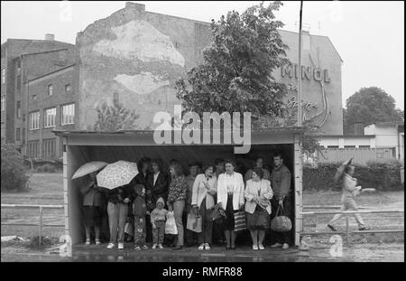 Deutschland, Berlin, 29. Mai 1990: Straßenbahnhaltestelle, Wartebereich, warten (DDR) Bürger auf der Suche nach Unterschlupf vor dem Regen (Tierheim), Werbung (DDR): "inol zur Spitze', Weißensee, Berlin. Stockfoto