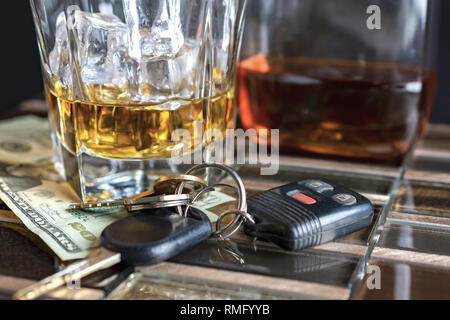 Alkohol in ein Glas mit Eis, Flasche im Hintergrund. Schlüssel und Geld im Vordergrund. Suggestive von trinken und fahren. Stockfoto