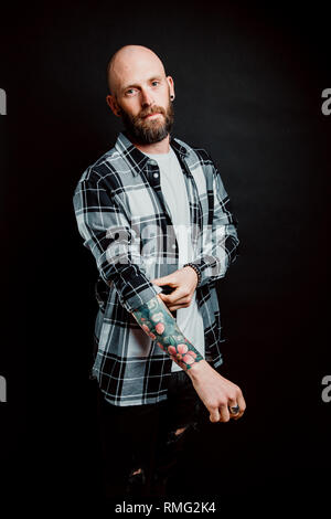 Bärtige haarlose Hipster in Shirt mit Tattoos auf Arme auf schwarzem Hintergrund Stockfoto