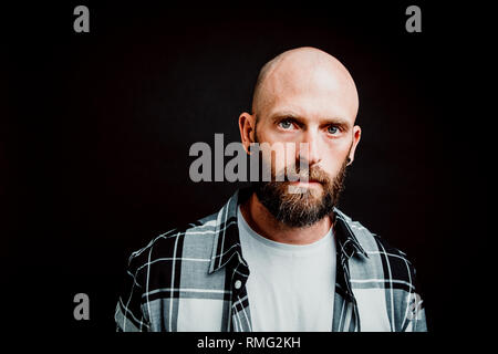 Bärtige haarlose Hipster in shirt Kamera schaut auf schwarzem Hintergrund Stockfoto