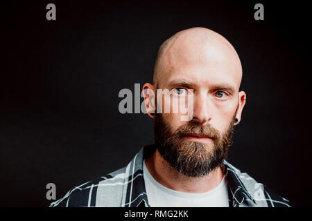 Bärtige haarlose Hipster in shirt Kamera schaut auf schwarzem Hintergrund Stockfoto