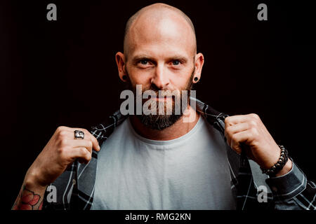 Bärtige haarlose Hipster in Shirt mit Tattoos auf Arme auf schwarzem Hintergrund Stockfoto