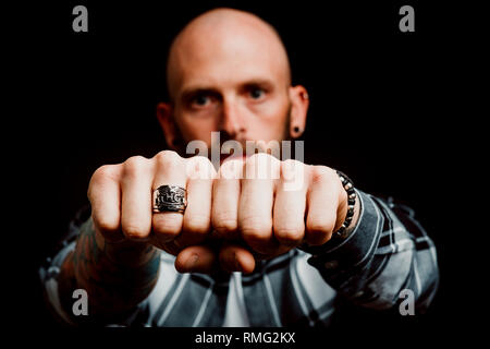 Bärtige ernste Hipster in Shirt mit Tattoos auf der Hand zeigen Fäuste mit Ring auf schwarzem Hintergrund Stockfoto