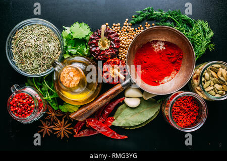 Von oben Satz von verschiedenen Gewürzen und Kräutern auf schwarzen Hintergrund platziert um eine Flasche Öl Stockfoto