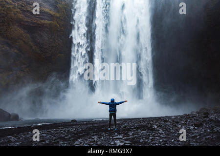 Eine Person admirnig die Schönheit der Skogafoss Wasserfall in Island entfernt Stockfoto