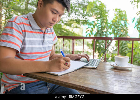 Asiatischer mann Schreiben von Notizen und mit Laptop Stockfoto