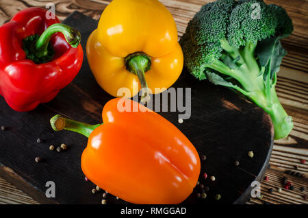 Saftig rot und orange Paprika mit einem grünen Schwanz liegt neben der Kopfsalat und Brokkoli zu Bündeln sind auf einem braunen Holztisch. Stockfoto