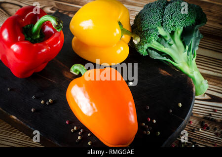 Saftig rot und orange Paprika mit einem grünen Schwanz liegt neben der Kopfsalat und Brokkoli zu Bündeln sind auf einem braunen Holztisch. Stockfoto