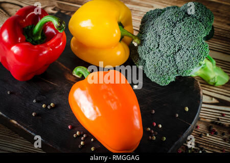 Saftig rot und orange Paprika mit einem grünen Schwanz liegt neben der Kopfsalat und Brokkoli zu Bündeln sind auf einem braunen Holztisch. Stockfoto