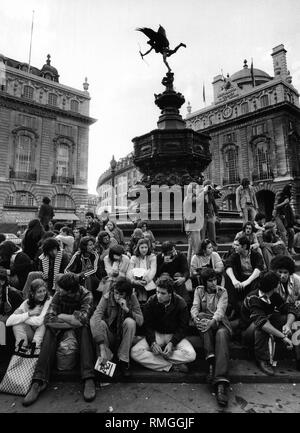 Touristen sitzen auf den Stufen des Shaftesbury Memorial Fountain am Piccadilly Circus in London. Stockfoto