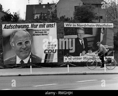 Zwei wahl Plakate für die Landtagswahl in Nordrhein-Westfalen am 12.5.1985 auf einer Straße. Auf der linken Seite ist ein Plakat der CDU mit der Inschrift: "die wirtschaftliche Erholung. Nur mit uns! Revival für die NRW-CDU". Neben einem Portrait von Helmut Kohl mit einem Zitat: "Vertrauen Bernhard Worms.". Direkt daneben ein Plakat der SPD. Es lautet: "Wir in Nordrhein-Westfalen und unser Minister Präsidenten'. Zusätzlich ein Bild von Johannes Raus. Ein Teil der Inschrift der Poster ist verdeckt von einem vorbeifahrenden Radfahrer. Stockfoto