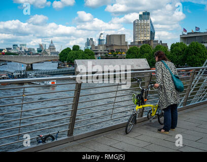 London, England - 2 Juni 2018: eine Dame mit Fahrrad prüft die Plakette auf der Golden Jubilee Fußgängerbrücke vom Southbank zu Charing Cross. Stockfoto