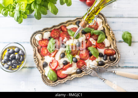Gießen Olivenöl auf Caprese Salat. Gesunde italienische und mediterrane Mahlzeit Stockfoto