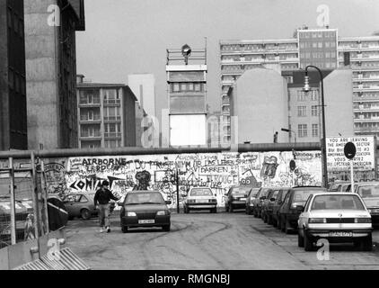 Ansicht des Graffiti-bedeckten Mauer in Berlin in der Kochstraße, Berlin-Kreuzberg. In der Mitte, ein Wachturm der DDR. Auf der rechten Seite ein Schild mit der Aufschrift "Sie verlassen den amerikanischen Sektor". Stockfoto