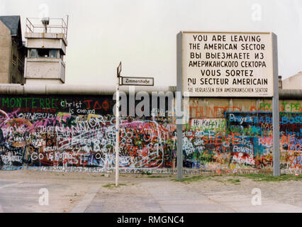 Dreisprachige Warnschild an der Sektorengrenze ("Sie verlassen den amerikanischen Sektor", Wand mit Graffiti und Wachturm in Berlin. Stockfoto