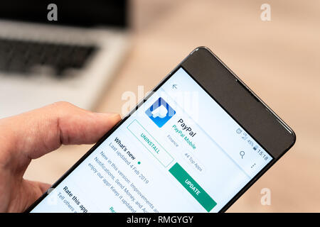 Die menschliche Hand Handy - paypal App im App Store, computer Laptop im Hintergrund. Slowenien 13.02.2019 Stockfoto