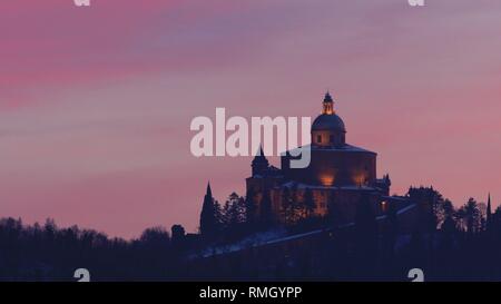 Fernsicht auf Heiligtum der Jungfrau von San Luca auf dem Colle della Guardia in Bologna. Dämmerung im Winter Schnee, rosa Himmel mit Platz kopieren. Hist Stockfoto