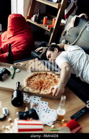 Betrunkener Mann schlafend auf dem Sofa in der Nähe lecker Pizza zu unordentlich Home nach Partei Stockfoto