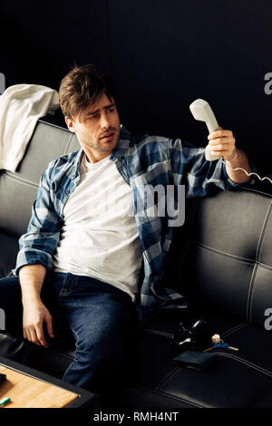 Betrunkener Mann an retro Telefon und Sitzen auf einem Sofa nach der Party zu Hause Stockfoto
