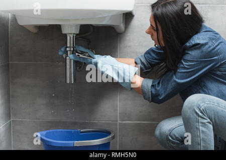 Brünette Frau in Gummihandschuhe Leitung reparieren Stockfoto