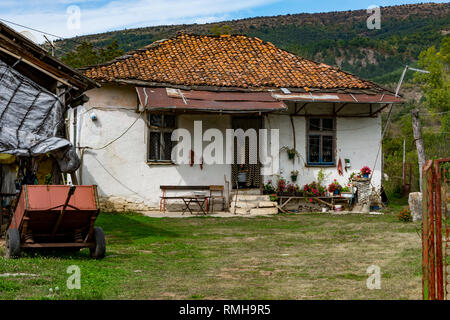 Alten, verfallenen Haus in der Ortschaft Slavinja, Oma steht auf der Terrasse und schaut. Getrocknete Chilis und Knoblauch sind an der Vorderseite der Tür hungin. Stockfoto
