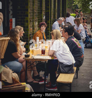 London, UK, 2018. Eine Gruppe von jungen Leuten Getränke außerhalb einen Pub in der Nähe von Columbia Road in Shoreditch. Stockfoto