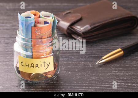 Glas Glas mit Münzen und Banknoten mit der Aufschrift LIEBE. Auf der alten schwarzen Holztisch. Das Konzept der Freundlichkeit und Hilfe. Stockfoto