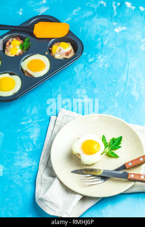 Gebackene Eier in der Licht- und Backformen. Portioniert Auflauf von Speck und Eier im italienischen Stil. Blauer Beton Tischfläche Hintergrund. Stockfoto
