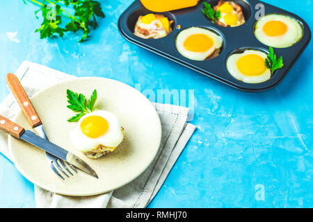 Gebackene Eier in der Licht- und Backformen. Portioniert Auflauf von Speck und Eier im italienischen Stil. Blauer Beton Tischfläche Hintergrund. Stockfoto