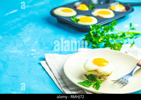Gebackene Eier in der Licht- und Backformen. Portioniert Auflauf von Speck und Eier im italienischen Stil. Blauer Beton Tischfläche Hintergrund. Stockfoto