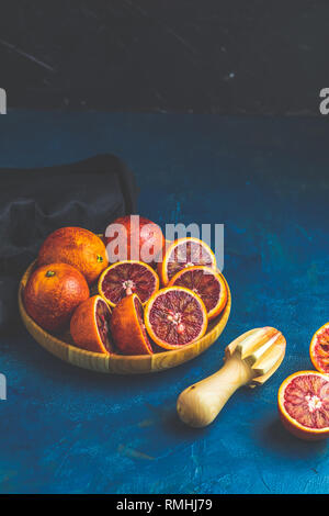 Sizilianische Hälfte Blutorangen gequetscht und Schnitt in Holz- Platte über Dunkelblau konkrete Tabelle Oberfläche gepresst. Dunklen rustikalen Stil. Stockfoto