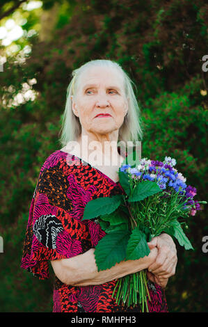 Ältere Großmutter mit einem Strauß Blumen im Park. Stockfoto