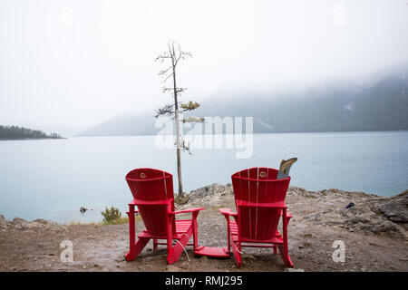 Zwei roten Stühlen mit Blick auf Lake Minnewanka an einem nebligen Tag in Banff National Park, Kanada Stockfoto