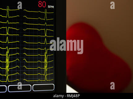 Bildschirm des Elektrokardiographen Geräts mit zwölf gelben EKG EKG-Rhythmus führt. Mit der Herzfrequenz. Ein rotes Herz Form auf einem verschwommenen Hintergrund Stockfoto