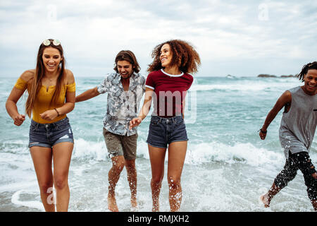 Freundliche Männer und Frauen zu Fuß am Strand. Multi-ethnischen junge Männer und Frauen zu Fuß auf Meer mit viel Spaß. Stockfoto