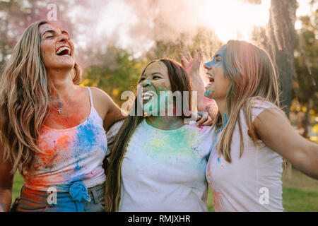 Drei Frauen Spaß Holi spielen mit Farben auf ihrem Gesicht spritzte. Freunde genießen Holi in einem Park und Lachen in der Freude. Stockfoto