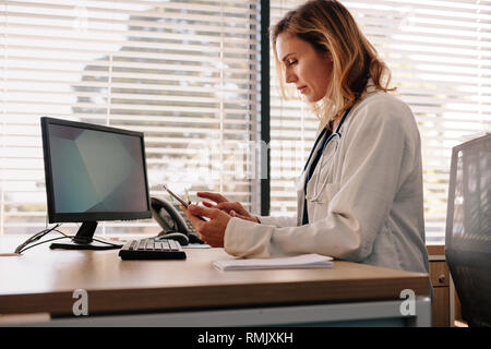 Weibliche Arzt mit Hilfe eines digitalen Tablet in der Klinik. Ärztin an ihrem Schreibtisch sitzen und arbeiten an Ihrem Tablet-PC in Ihrem Büro. Stockfoto