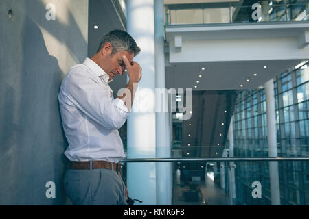 Betonte Geschäftsmann an die Wand gelehnt im Büro Stockfoto