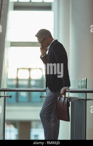 Geschäftsmann mit Aktenkoffer, am Telefon zu sprechen und lehnte sich auf dem Geländer Stockfoto