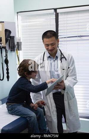 Jungen asiatischen männlicher Arzt und kaukasische junge Patienten mit digitalen Tablet in der Klinik Stockfoto