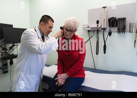 Jungen Asiatischen männlicher Arzt prüft ein älterer Patient in der Klinik Stockfoto